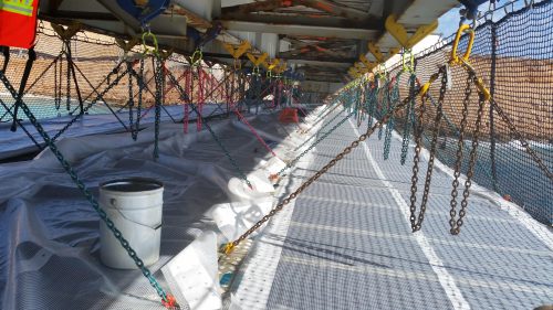 A walkway of tension netting attached to the underside of a bridge with chains has been installed.