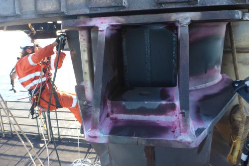 A rope access NDT technician conducting Dye Penetrant inspection (DPI) on an offshore structure.