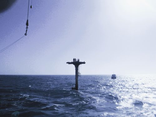 Two technicians stand on a small platform in the waters around the chevril platform.