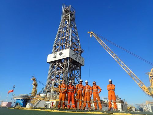 A group of Vertech technicians pose for a photo with a derrick and crane in the background.