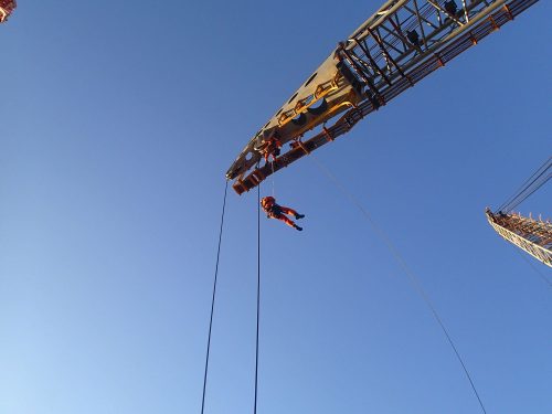 A vertech IRATA rope technician lowering themselves off the arm of a crane while a team member prepares to join them.