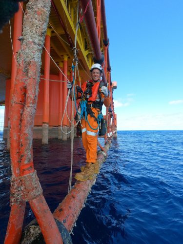 A Vertech IRATA Rope Access Technician stands on a support beam on the section of CPF that meets the water.