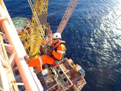 A vertech IRATA Rope Access Technician hangs suspended from the side of an FPSO, water visible below.