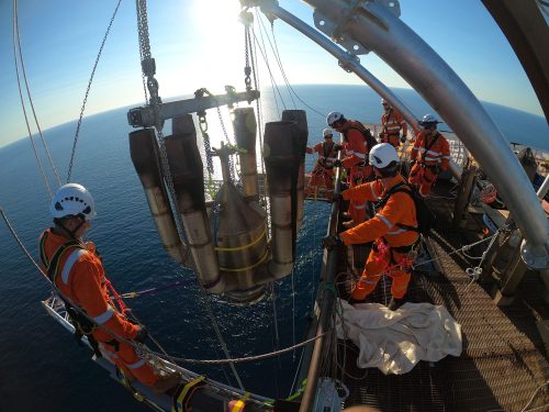 Vertech IRATA Rope Access Technicians are lowering an old flare tip off the side of the flare tower on an FPSO. Ocean in the background.
