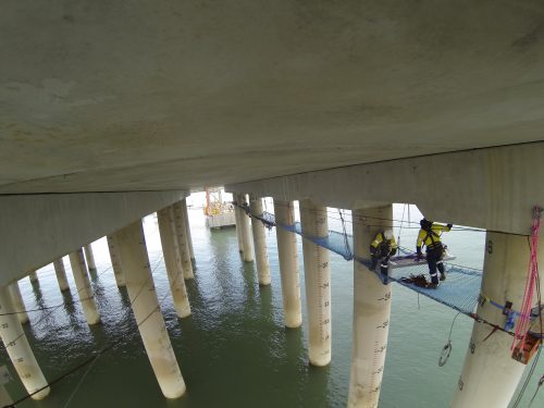 Two Vertech IRATA rope access technicians are installing the tension netting under the Gladstone LNG facility.