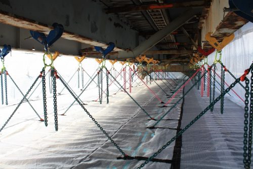 The fully installed netting on the underside of the bridge, chains criss cross the view directly down the platform.loading=