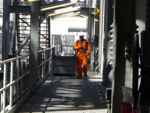 A Vertech technician stands at the end of a metal grate galley on the Ichthys Venturer FPSO.