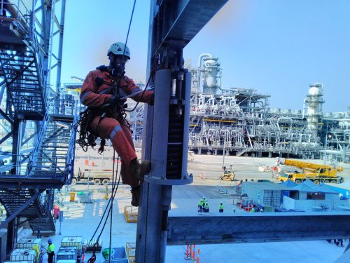 A vertech IRATA Rope access technician hangs suspended from ropes with a wrench in hand while constructing the INPEX LNG plant.