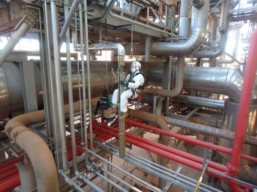 A vertech IRATA Rope Access Technician dressed in full white protective suit is suspended via rope to carry out inspections on a designated part of the KGP facility.