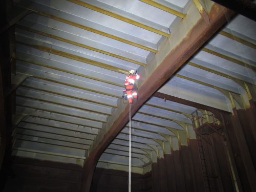 A Vertech IRATA Rope Access technician is is testing a pipe running along the roof of the hull.