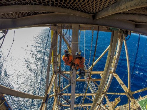 Two vertech technicians suspended under the facility platform performing testing on a support beam going down into the ocean.