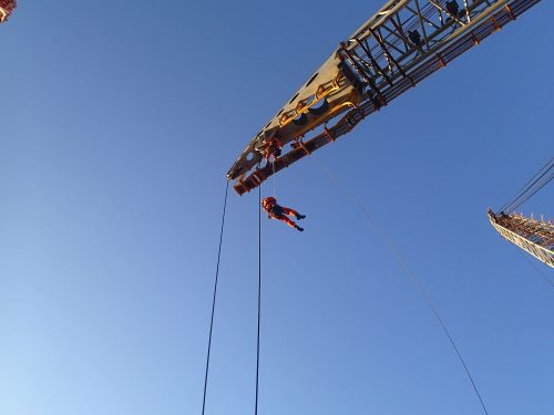 A vertech IRATA rope access technician hangs from the arm of an offshore crane as part of an integrity testing service.