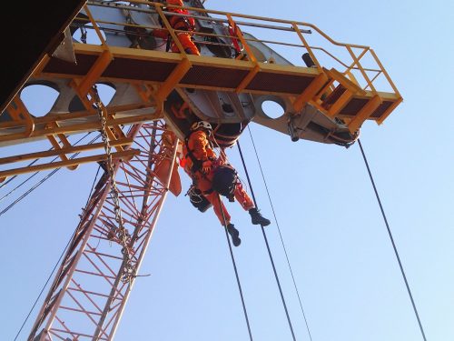 A vertech IRATA rope access technician hangs from the arm of an offshore crane as part of an integrity testing service.