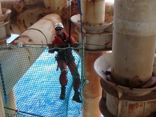 A Vertech Technician stands on the installed tension netting over the ocean.loading=