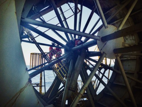 Two vertech technicians stand on a large mechanism within the Ningaloo vision FPSO.