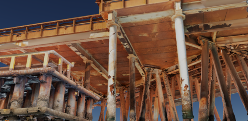 The image is a 3D rendering showing the detailed understructure of an offshore platform. The focus is on the corroded metal beams and pillars that form the substructure, with the textures and colouration suggesting advanced stages of rust and material degradation. Above, the platform’s deck is visible, providing a sharp contrast to the worn conditions of the support elements below. The perspective offers a clear view of the engineering complexity and maintenance challenges faced in the harsh marine environment. The visualisation technique provides clarity and depth, highlighting areas of concern for structural integrity assessments.