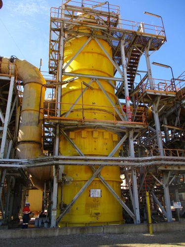 A large yellow cylindrical piece of refinery equipment covered in scaffolding. A large yellow cylindrical piece of refinery equipment covered in scaffolding.