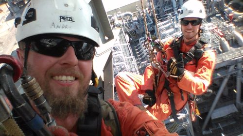 A vertech IRATA Rope Access technician is taking a selfie with another tech while suspended off the facility's side.