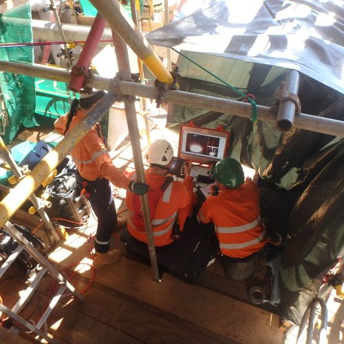 Three Vertech technicians huddled around an electronic screen hooked up to the camera of an RDVI crawler in a pipe.