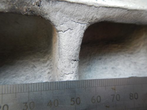 A metal ruler is used to measure the size of cracks in a concrete support system.loading=