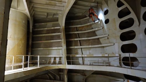 A vertech IRATA rope access NDT technician inspects the wall of a hull while suspended on ropes.