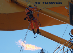 IRATA-trained rope access technician performing inspection work on industrial equipment in Perth, suspended from a crane boom with safety gear and harness in clear weather conditions.