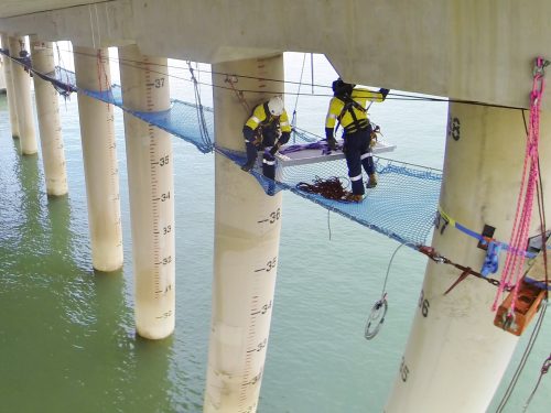 IRATA rope access technicians installing a tension netting system on a coastal jetty to complete concrete inspection and remediation.