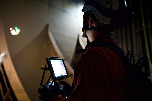 A Vertech drone operator uses an electronic tablet to control a lit-up drone.