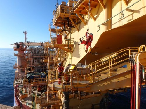 Two Vertech technicians, one suspended by ropes and one standing below conduct testing on an fpso.