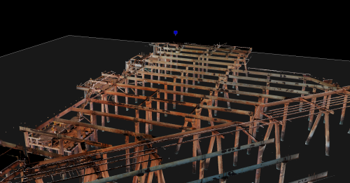 This image presents a 3D rendering of a complex offshore platform structure, viewed from an angle that captures its expansive frame. The steel beams and support network are shown in various weathering states, indicative of a marine environment. Despite the dark background that suggests this could be an isolated section from a larger model, the intricacy of the architecture is evident, showing multiple levels and an array of pipes and platforms that make up the industrial facility. There are no visible workers or equipment, pointing to a focus on the structure itself, possibly for analysis, planning, or digital documentation purposes. The blue pinpoint at the top centre implies a specific area of interest or a reference point within the 3D model.