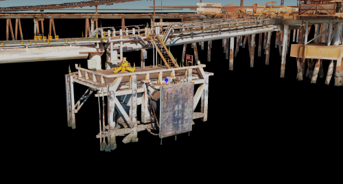 The image displays a 3D render of an offshore structure and jetty with intricate metal beams and pipe framework. The image focuses on a suspended platform, also known as a diving stage or basket, used for transporting workers or equipment to lower levels or into the water. The platform is fitted with various tools and equipment, indicating active work. Visible signs label a "Pile 4," suggesting ongoing construction or maintenance. The structure shows signs of weathering and rust, typical for marine environments. The clear sky in the background contrasts with the complexity of the industrial setup, and no people are visible, which implies either automated processes or that the work is currently halted.